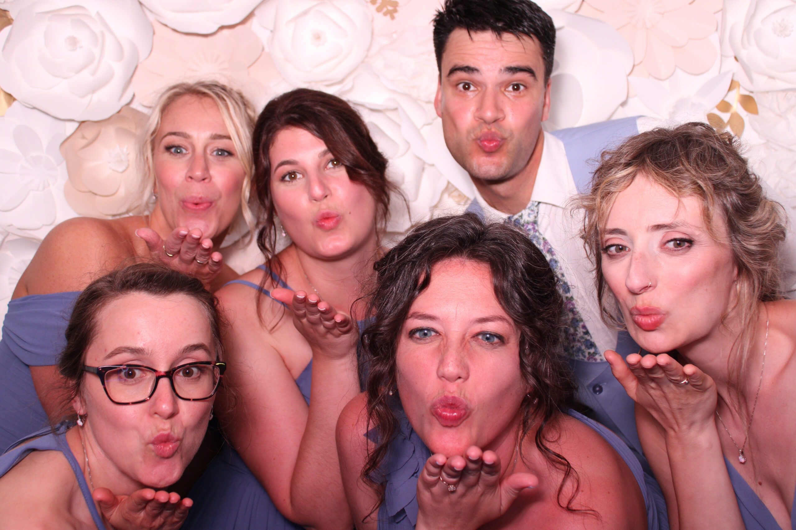 group of bridesmaids in wedding photo booth posing in front of white flower wall