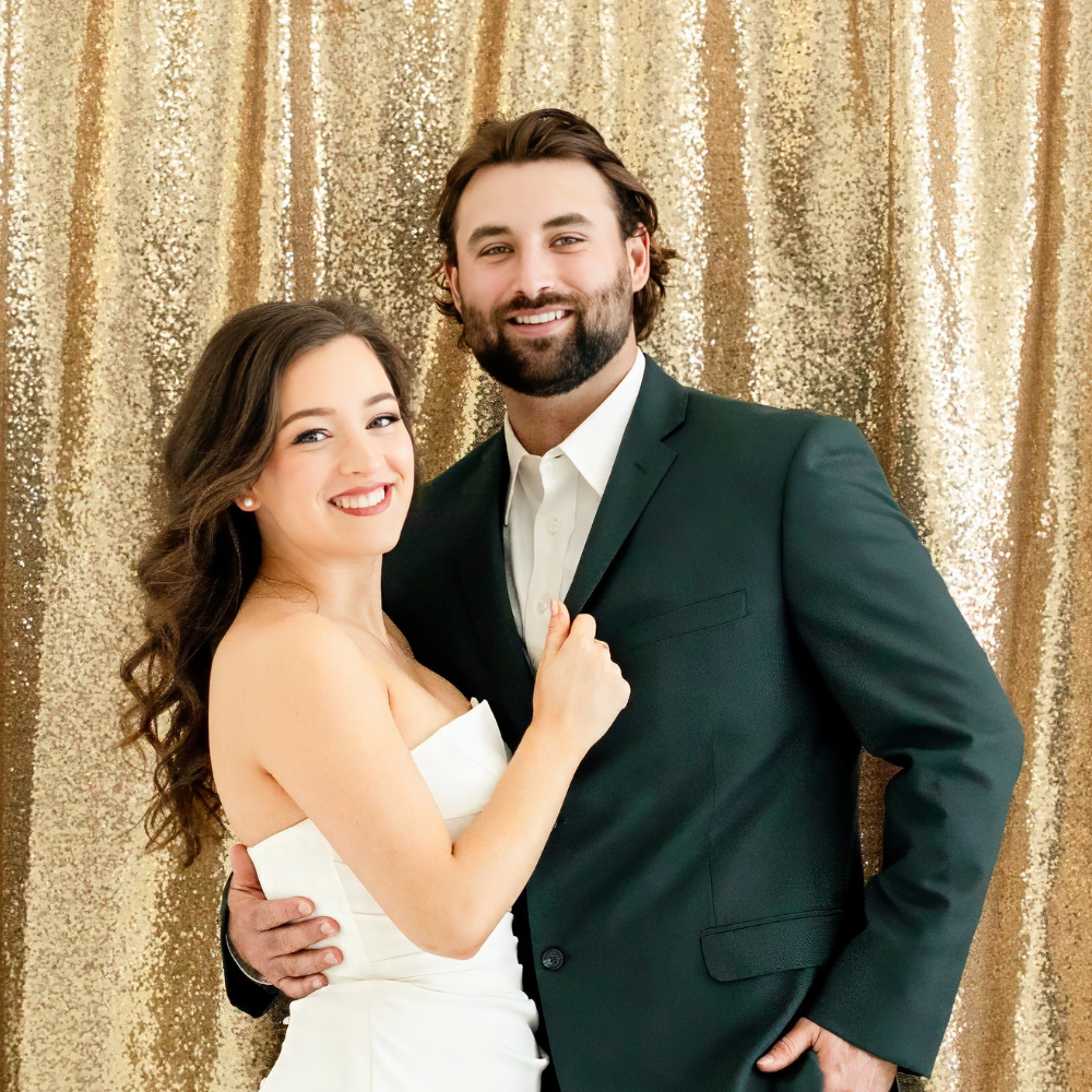 Bride and groom posing in front of gold sequin backdrop during wedding reception photo booth