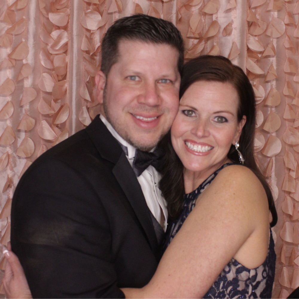 couple posing in photo booth with pink petal backdrop for Valentine's Day party