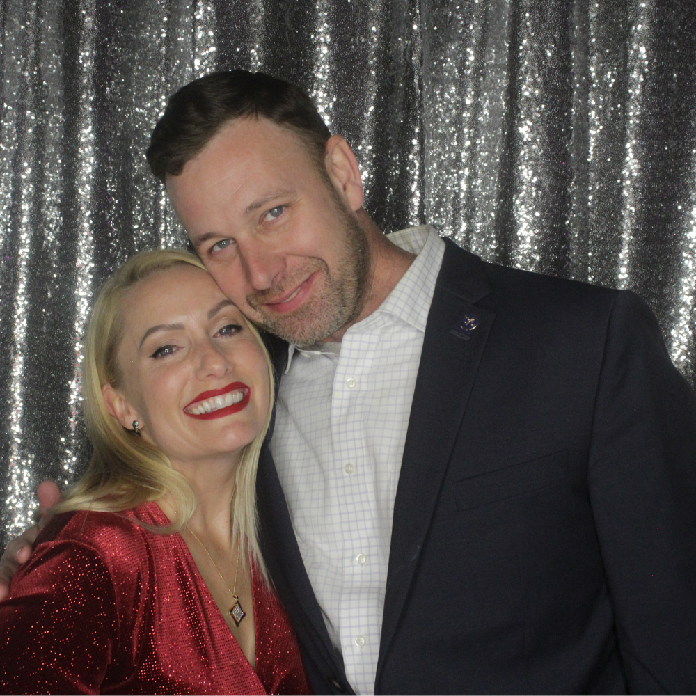 man and woman posing in front of silver sequin backdrop at holiday party photo booth