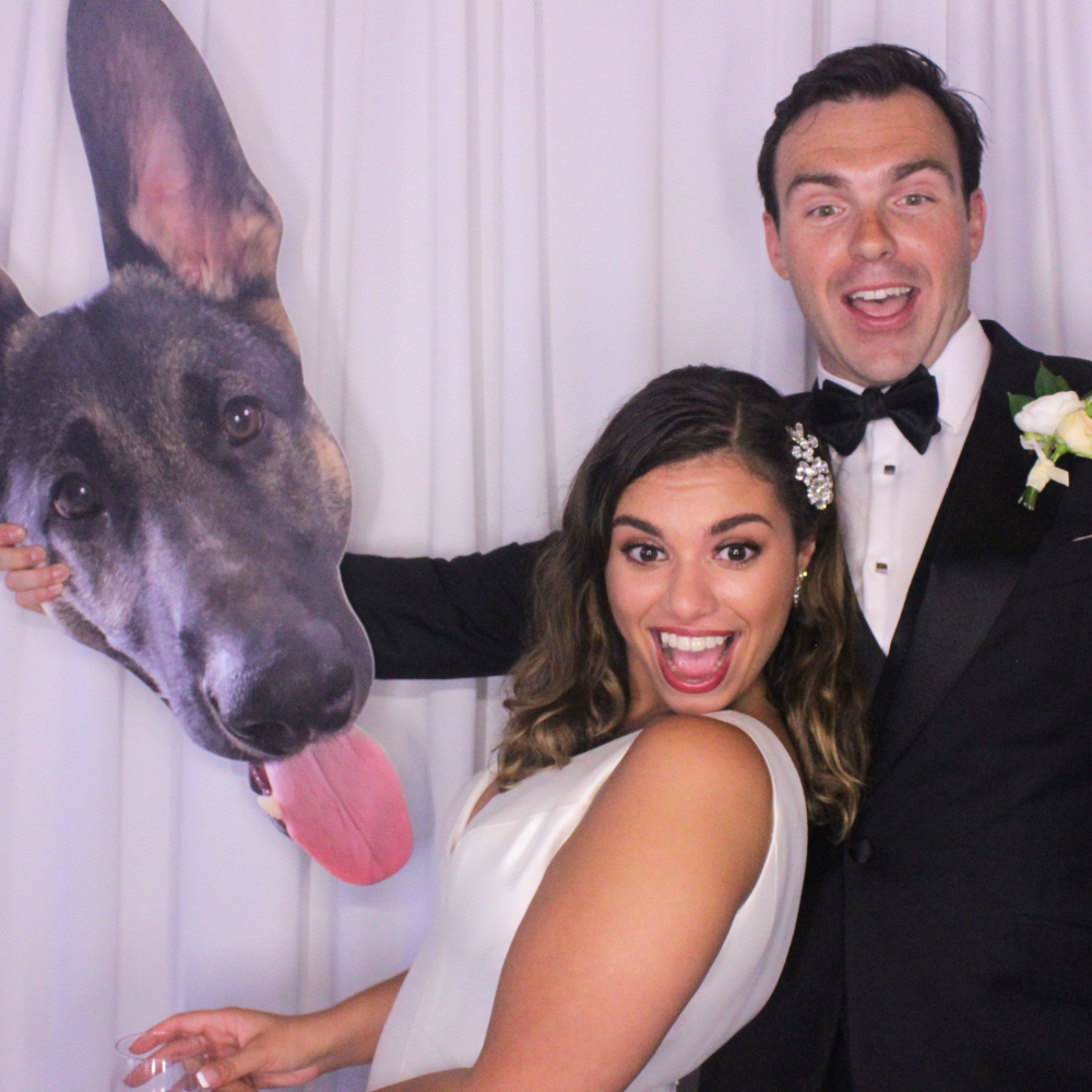 newlyweds in wedding photo booth posing with dog prop in front of white background