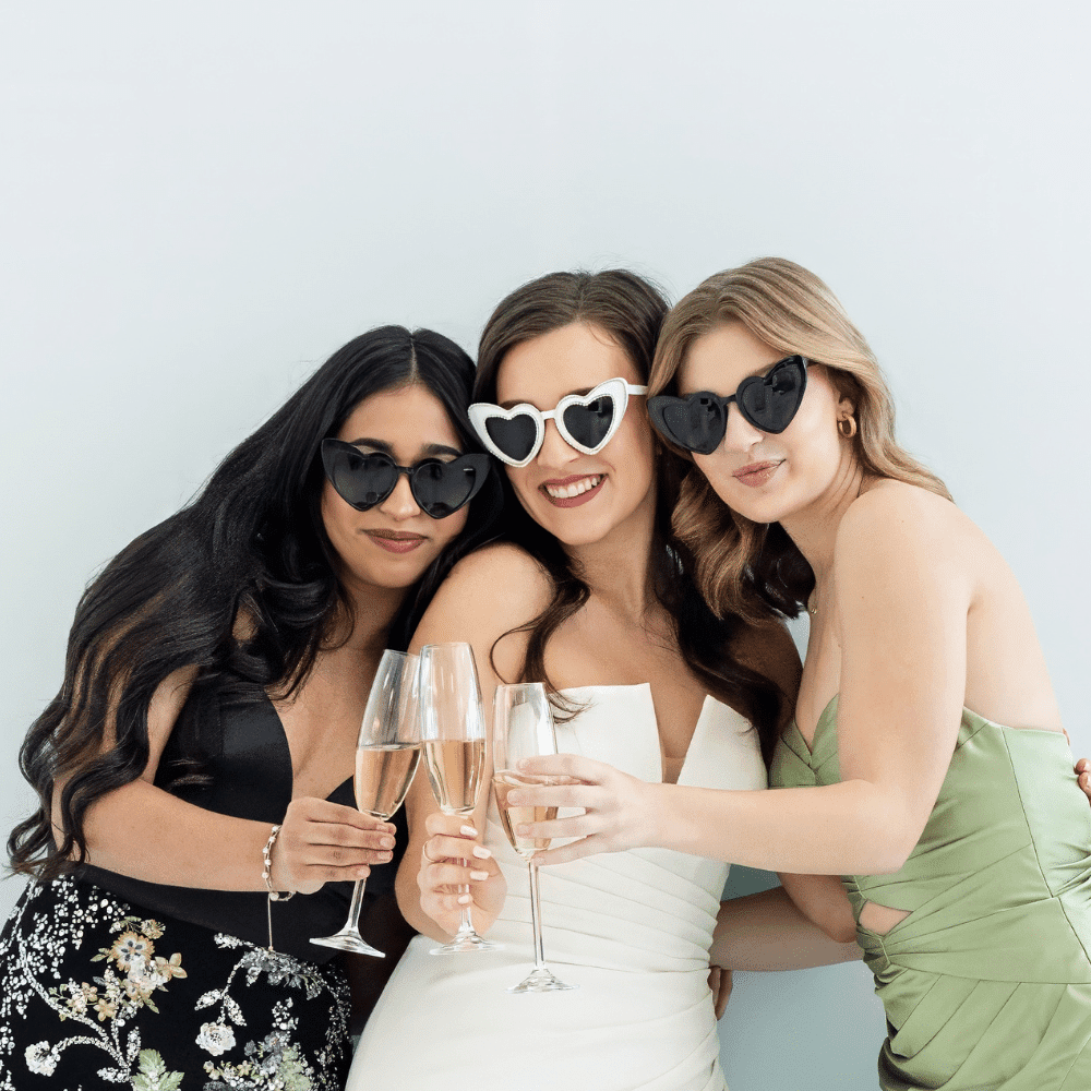 bride and bridesmaids posing in front of white backdrop with open air photo booth at wedding reception