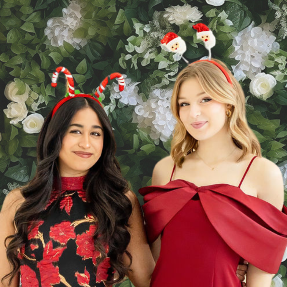 two girls posing in party photo booth in front of a white flower with greenery backdrop