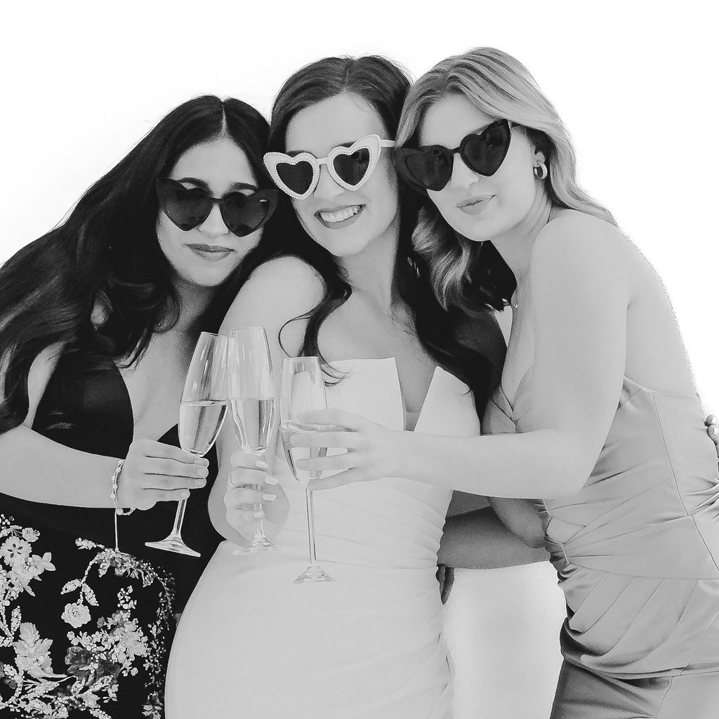 088A0913-2 (1) black and white glam photo booth photo of bride with two bridesmaids toasting with champagne classes and wearing heart sunglasses