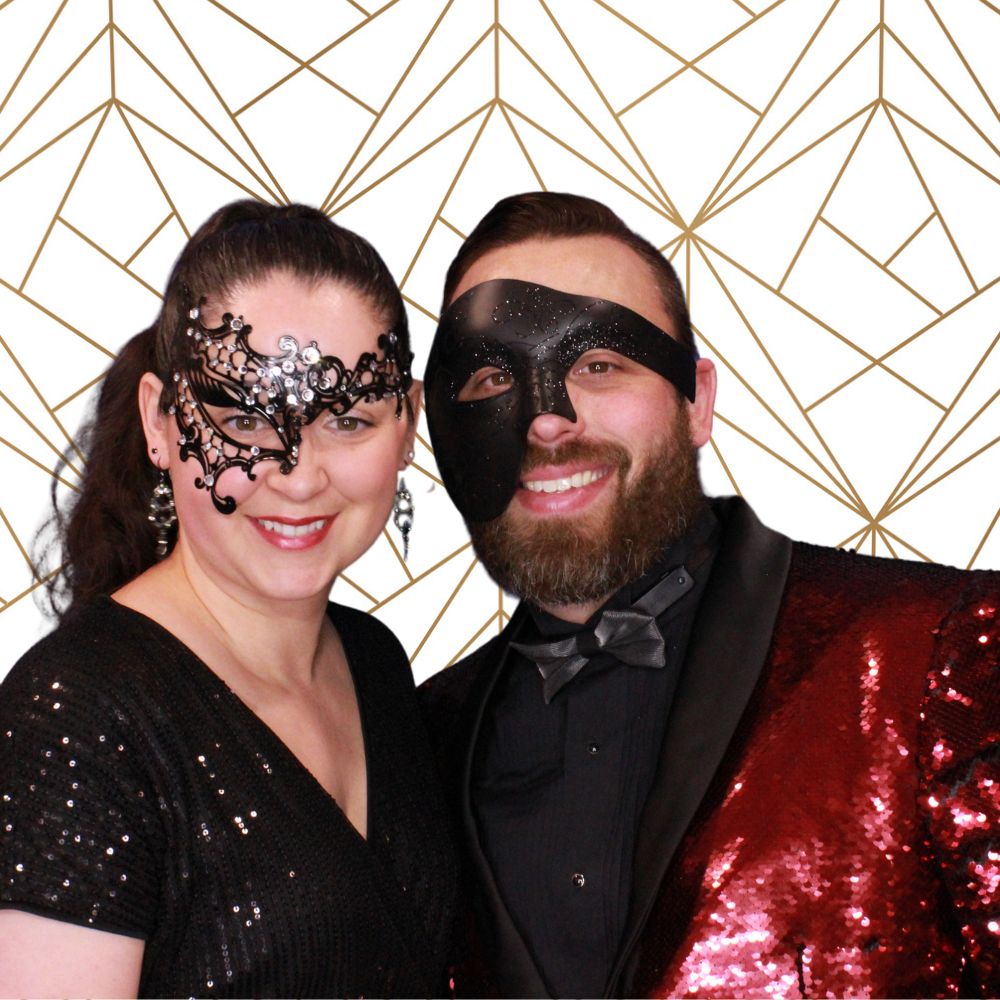 white-gold-geometric-background-couple(1000 x 1000 px) woman and man wearing masks posing in front of white with gold geometric shapes backdrop at holiday party photo booth